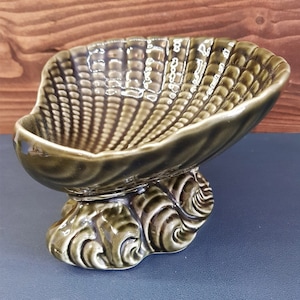May include: A green ceramic seashell dish with a wavy base. The dish is glazed and has a glossy finish.
