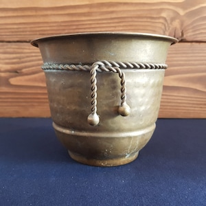 May include: A brass planter with a rope trim and decorative metal balls. The planter has a hammered finish and is a vintage style.