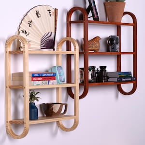 May include: Two wooden wall shelves with rounded edges. The top shelf is dark brown wood and the bottom shelf is light wood. The shelves are decorated with books, a fan, a bowl, a bird figurine, binoculars, and a camera.