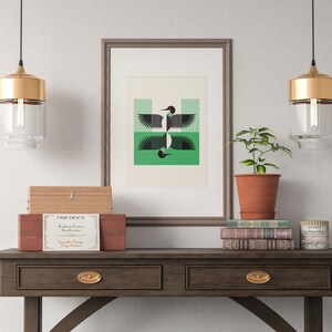 Peut inclure: Une impression encadr&eacute;e d'un motif d'oiseau g&eacute;om&eacute;trique noir et vert est suspendue au-dessus d'une console en bois avec deux tiroirs. La table a des poign&eacute;es de tiroir dor&eacute;es et est d&eacute;cor&eacute;e d'une bo&icirc;te en bois, d'une plante en pot et d'une pile de livres.