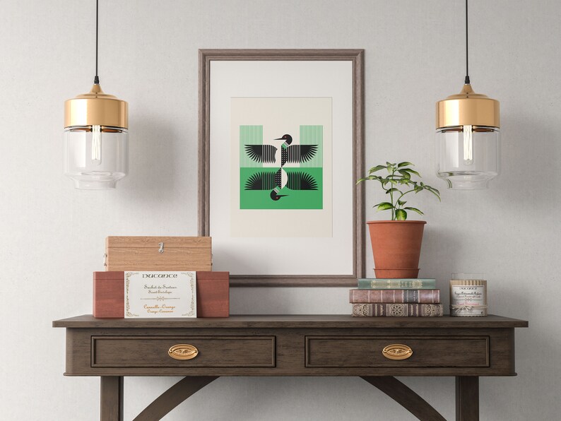 Peut inclure: Une impression encadr&eacute;e d'un motif d'oiseau g&eacute;om&eacute;trique noir et vert est suspendue au-dessus d'une console en bois avec deux tiroirs. La table a des poign&eacute;es de tiroir dor&eacute;es et est d&eacute;cor&eacute;e d'une bo&icirc;te en bois, d'une plante en pot et d'une pile de livres.