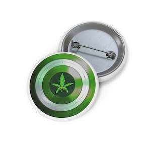 May include: A green and white button featuring a stylised marijuana leaf in the centre. The button is designed to resemble a superhero shield.