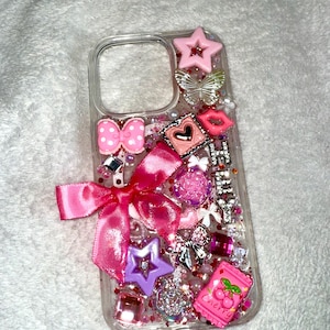 May include: Clear phone case decorated with pink bows, stars, and a cherry candy charm. The case is embellished with glitter and various charms, creating a playful and girly aesthetic.