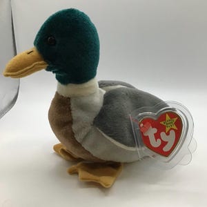 May include: A plush mallard duck toy with a green head, yellow beak, and gray and brown body. The toy has a red heart-shaped tag attached. A classic collectible toy.