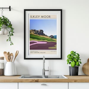 May include: A black framed poster with a minimalist illustration of a landscape. The poster has the text "ILKLEY MOOR" in a white sans-serif font. The text "WEST YORKSHIRE, ENGLAND" is below the illustration in a smaller font.