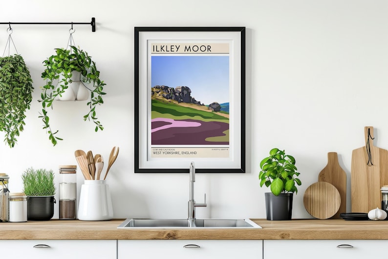 May include: A black framed poster with a minimalist illustration of a landscape. The poster has the text "ILKLEY MOOR" in a white sans-serif font. The text "WEST YORKSHIRE, ENGLAND" is below the illustration in a smaller font.