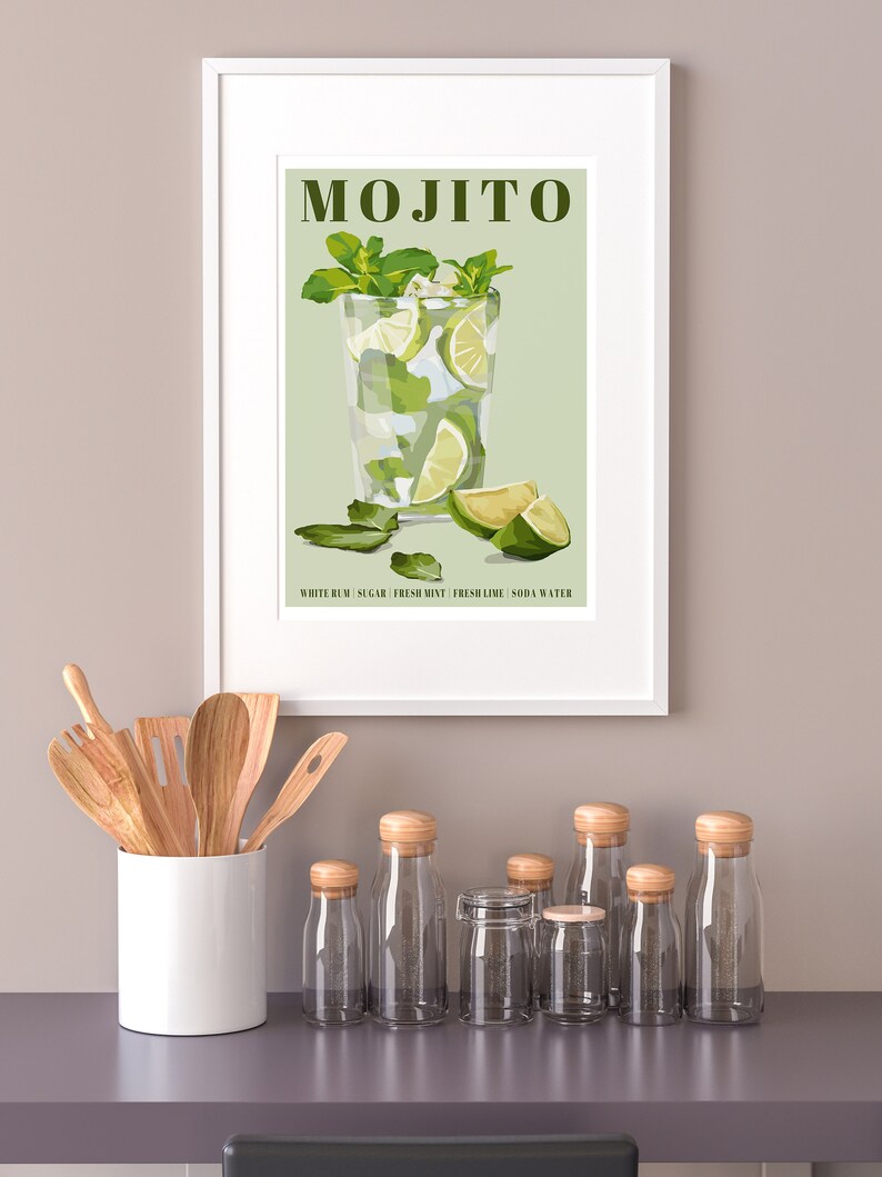 May include: A framed illustration of a mojito cocktail with the text "MOJITO" and "WHITE RUM | SUGAR | FRESH MINT | FRESH LIME | SODA WATER" on a green background. The illustration is surrounded by a white frame and is hanging on a light beige wall.