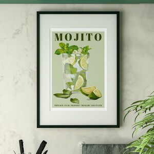 May include: A framed print with a green background featuring a glass of mojito with lime wedges and mint leaves. The text "MOJITO" is at the top of the print. The text "WHITE RUM, SUGAR, FRESH MINT, FRESH LIME, SODA WATER" is at the bottom of the print.