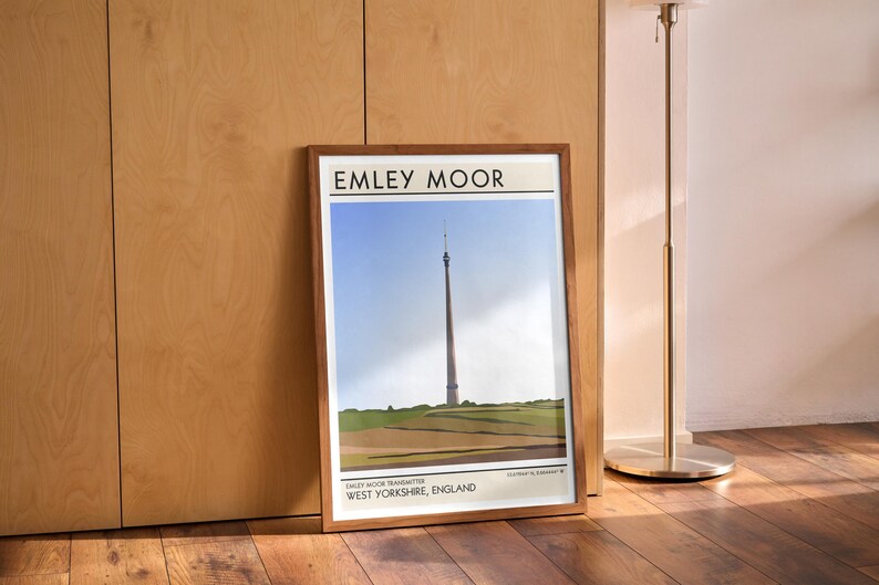 May include: A framed print of a minimalist illustration of the Emley Moor Transmitter, a tall tower in West Yorkshire, England. The print has a white background with black text and a brown frame.