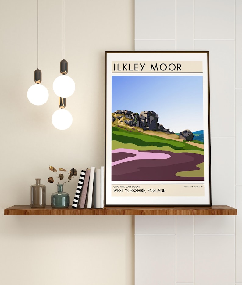 May include: A minimalist poster with a brown frame featuring a colorful illustration of Cow and Calf Rocks in Ilkley Moor, West Yorkshire, England. The poster has the text "ILKLEY MOOR" in a bold, sans-serif font at the top and "COW AND CALF ROCKS WEST YORKSHIRE, ENGLAND" at the bottom.