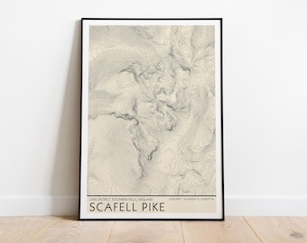 May include: A framed topographic map print of Scafell Pike in the Lake District, Southern Fells, England. The print features beige and grey contour lines, with the text "LAKE DISTRICT, SOUTHERN FELLS, ENGLAND" and "SCAFELL PIKE" at the bottom.
