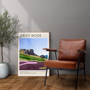 May include: A brown leather armchair with a black metal frame sits in front of a framed print of a landscape scene. The print features a stylized illustration of a rocky hill with the text "Ilkley Moor" and "Cow and Calf Rocks, West Yorkshire, England" at the bottom.
