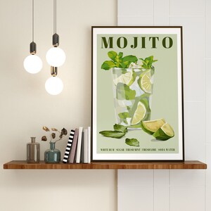 May include: A framed print with a green background and a glass of mojito with lime wedges and mint leaves. The text "MOJITO" is at the top of the print. The text "WHITE RUM | SUGAR | FRESH MINT | FRESH LIME | SODA WATER" is at the bottom of the print.