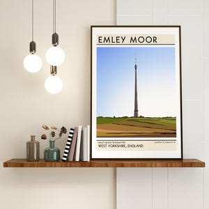 May include: A minimalist illustration of the Emley Moor Transmitter, a tall, slender tower with a red and white color scheme, set against a blue sky and green hills. The text "Emley Moor" is at the top of the image, and "Emley Moor Transmitter, West Yorkshire, England" is at the bottom.