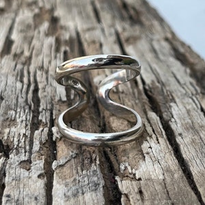 May include: A silver ring with a double band design. The ring is made of two bands that are connected in the middle, creating a unique and modern look.
