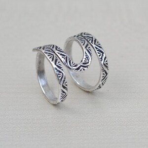 May include: Silver ring with a double-spiral design. The ring is decorated with a geometric pattern.