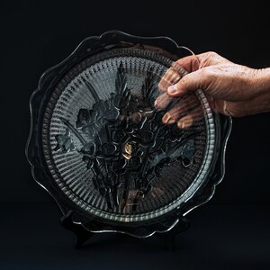 May include: A clear glass serving dish with a floral design. The dish is on a black stand and has a scalloped edge.