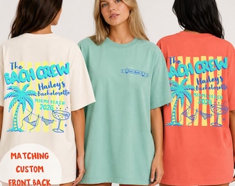 May include: Three short-sleeve t-shirts in cream, sage green, and coral. The cream and coral shirts feature a back graphic with a palm tree, bikini, cocktail glass, and text reading The BACH CREW Hailey's Bachelorette Miami Beach 2026.