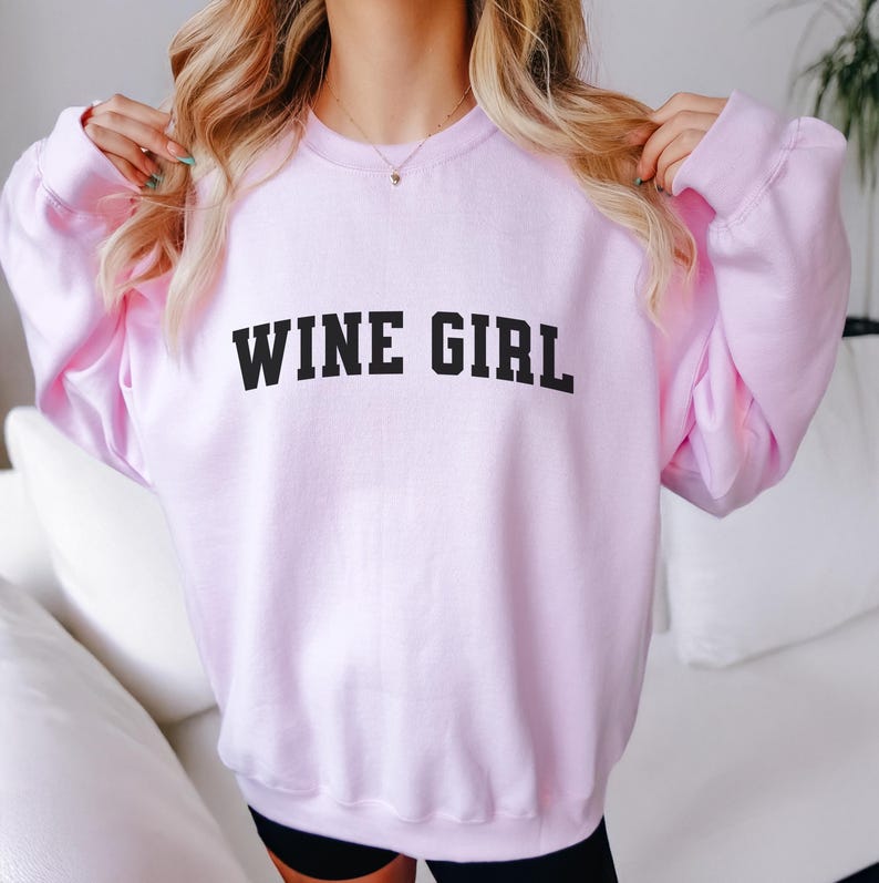 Pu&ograve; includere: Una felpa rosa con la scritta "WINE GIRL" stampata in nero.