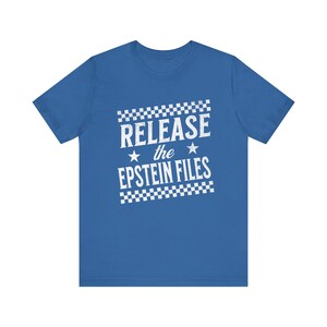 May include: Royal blue t-shirt with white text that reads "RELEASE the EPSTEIN FILES". The text is in a bold, sans-serif font, with a checkered pattern above and below the text. Two stars are present.