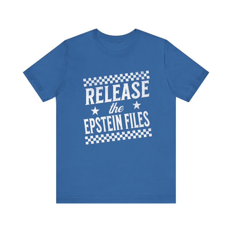 May include: Royal blue t-shirt with white text that reads "RELEASE the EPSTEIN FILES". The text is in a bold, sans-serif font, with a checkered pattern above and below the text. Two stars are present.