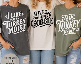 May include: Three short-sleeve crew neck t-shirts in charcoal, cream, and olive green. The charcoal shirt features the text 'I LIKE MY TURKEY MOIST', the cream shirt says 'GIVE ME SOMETHING TO GOBBLE', and the olive green shirt reads 'TALK TURKEY TO ME'.
