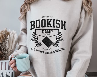 May include: A light gray sweatshirt with a black graphic print that says "Bookish Camp Est. 1989" with a wreath of leaves and the text "All Things Books & Reading".