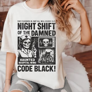 May include: Off-white t-shirt with a black and white graphic depicting a skull nurse, a skull on a monitor, and a wheelchair. Text reads "NIGHT SHIFT OF THE DAMNED" and "CODE BLACK!" in a spooky, gothic font.