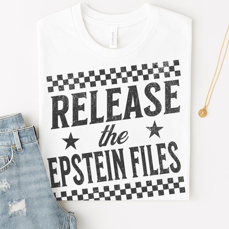May include: White t-shirt with the text "RELEASE the EPSTEIN FILES" in black, with a checkered pattern above and below the text. A pair of blue jeans and a gold necklace are partially visible.
