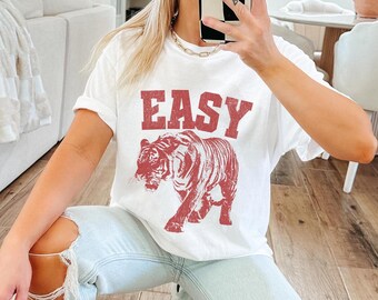 May include: White t-shirt with a red tiger graphic and the word "EASY" printed in red letters.