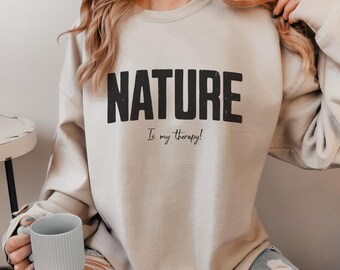May include: A light beige sweatshirt with the text "NATURE Is my therapy!" printed in black.