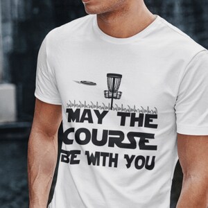May include: White t-shirt with a black graphic of a disc golf basket and disc with the text "May the course be with you".