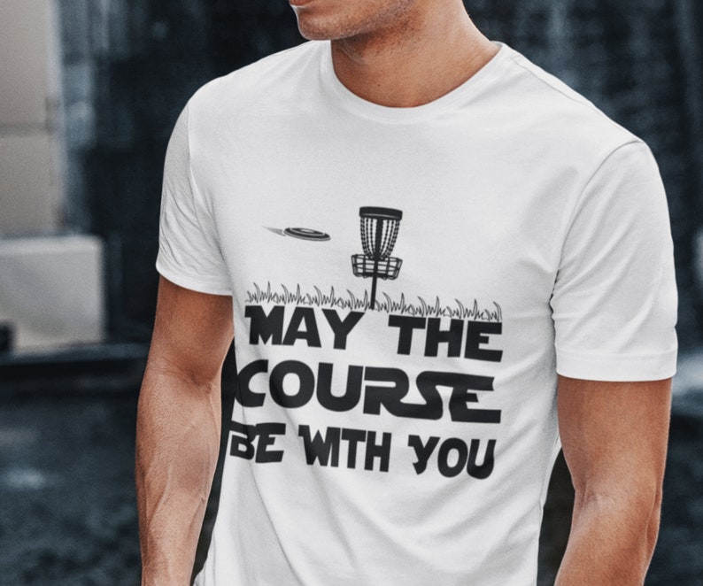 May include: White t-shirt with a black graphic of a disc golf basket and disc with the text "May the course be with you".