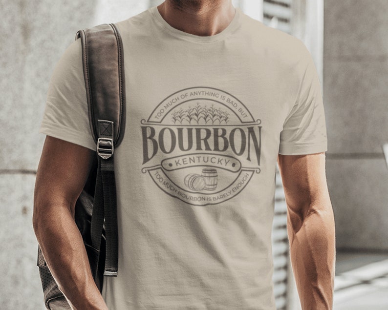 May include: A beige t-shirt with a circular graphic design featuring the text "Bourbon Kentucky" and the phrase "Too much of anything is bad, but too much bourbon is barely enough".