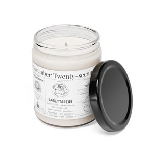May include: A white candle in a clear glass jar with a black lid. The label reads "November Twenty-second" and features the Sagittarius zodiac sign, along with characteristics like "optimistic" and "adventurous."