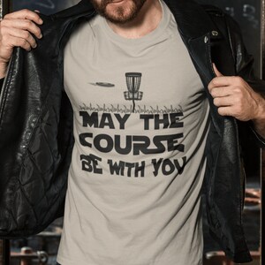 May include: A grey t-shirt with a black disc golf basket and the text "May the Course Be With You".