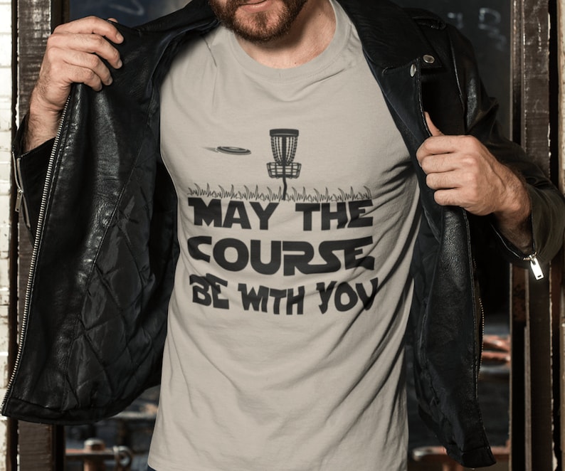 May include: A grey t-shirt with a black disc golf basket and the text "May the Course Be With You".