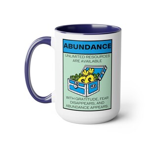 May include: White ceramic coffee mug with a blue rim. The mug features a cartoon illustration of a treasure chest overflowing with money bags and the text "ABUNDANCE, UNLIMITED RESOURCES ARE AVAILABLE, WITH GRATITUDE, FEAR DISAPPEARS, AND ABUNDANCE APPEARS."