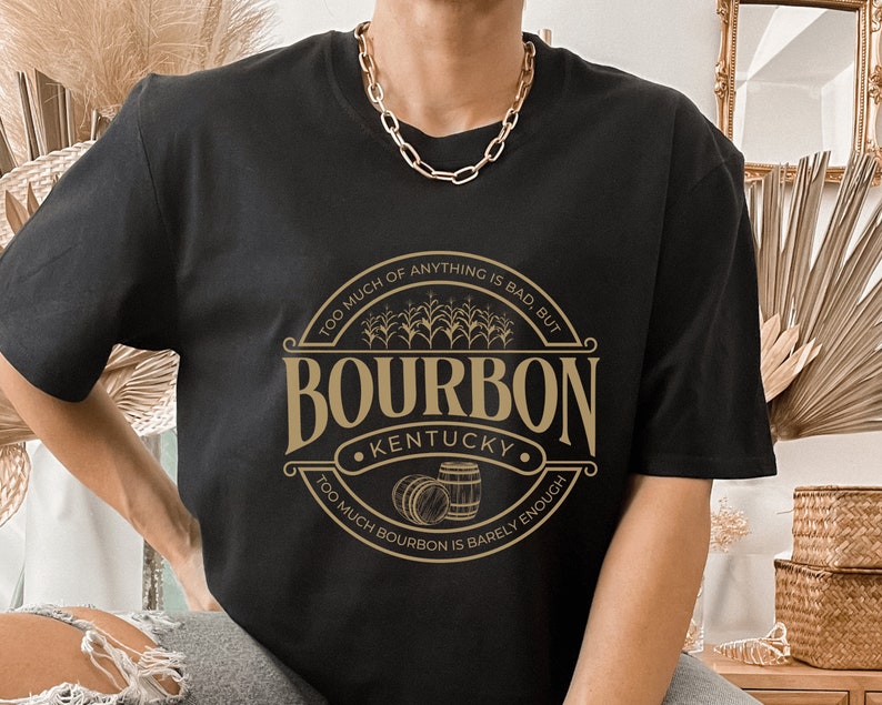 May include: Black t-shirt with a gold graphic of a bourbon logo. The logo says "Too much of anything is bad, but Too much bourbon is barely enough." and "Bourbon Kentucky".