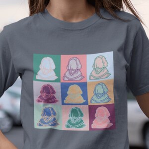 Puede incluir: Una camiseta gris oscuro con un estampado gr&aacute;fico colorido de nueve retratos diferentes de un hombre con barba y un cuello de encaje. Los retratos est&aacute;n dispuestos en una cuadr&iacute;cula de 3x3.