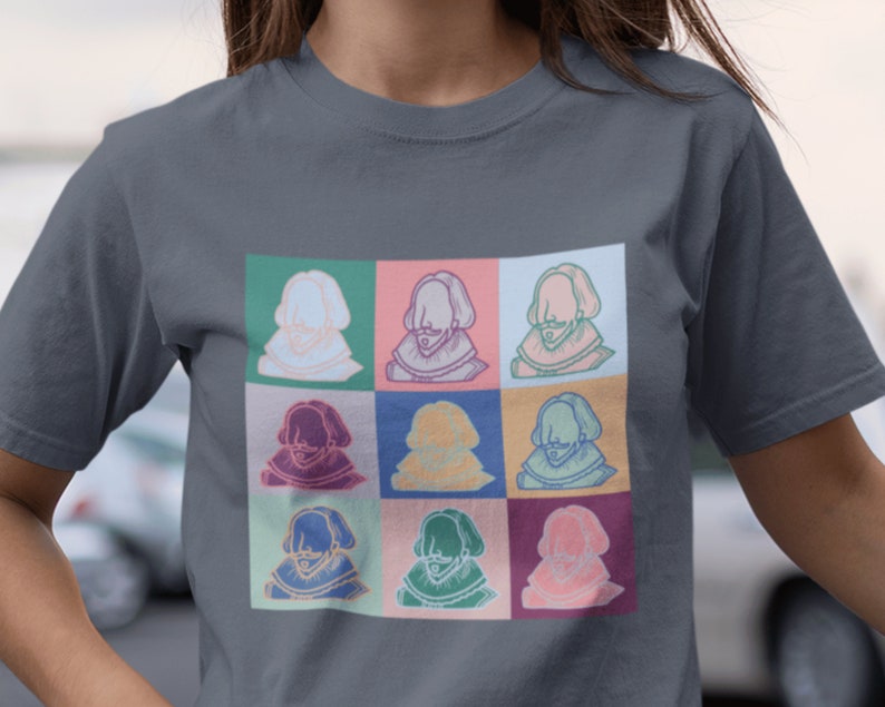 Puede incluir: Una camiseta gris oscuro con un estampado gr&aacute;fico colorido de nueve retratos diferentes de un hombre con barba y un cuello de encaje. Los retratos est&aacute;n dispuestos en una cuadr&iacute;cula de 3x3.