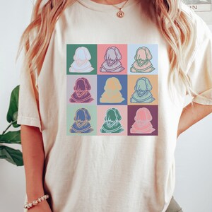 Puede incluir: Una camiseta blanca con un gr&aacute;fico colorido de la cara de un hombre repetido nueve veces. Cada cara est&aacute; delineada en negro y tiene un fondo de color diferente.