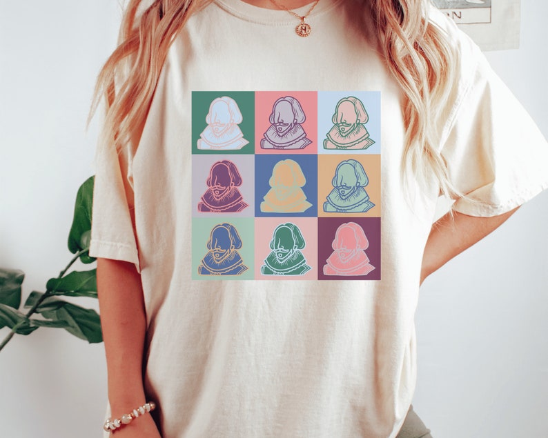 Puede incluir: Una camiseta blanca con un gr&aacute;fico colorido de la cara de un hombre repetido nueve veces. Cada cara est&aacute; delineada en negro y tiene un fondo de color diferente.