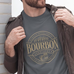 May include: A dark gray t-shirt with a gold graphic of a bourbon barrel and the text "Too much of anything is bad, but Too much bourbon is barely enough. Kentucky."