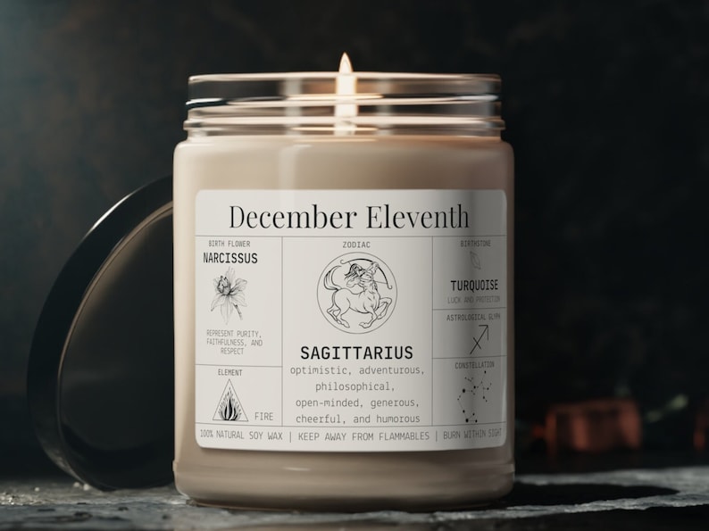May include: A lit candle in a glass jar with a label that reads "December Eleventh" and "Sagittarius." The label includes zodiac details, birth flower, and gemstone information. The candle is made with 100% natural soy wax.