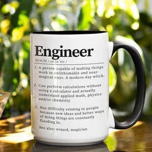 May include: White ceramic mug with a black handle. The mug has a black rim and features a humorous definition of the word "Engineer" in black text.