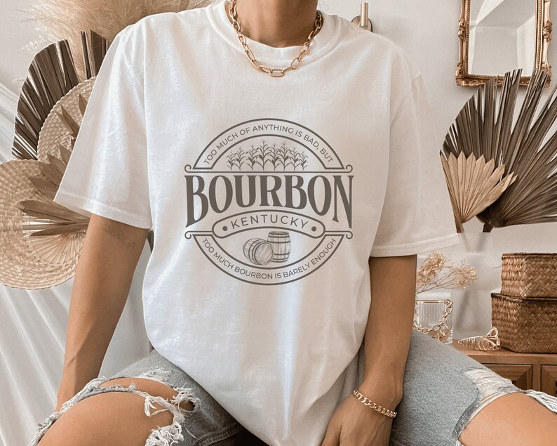 May include: White t-shirt with a brown graphic design that says "Bourbon Kentucky" with two barrels and the text "Too much of anything is bad, but too much bourbon is barely enough."