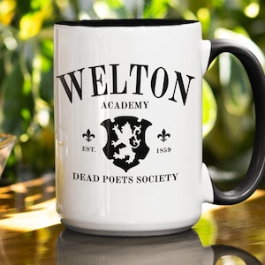 May include: White ceramic mug with a black handle. The mug has a black design that says "Welton Academy" with a lion crest and the text "Dead Poets Society".