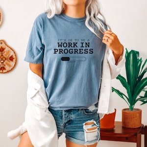 May include: A blue t-shirt with the text "It's ok to be a work in progress" and a loading bar graphic. The text "Loading..." is below the bar.
