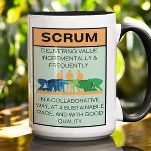 May include: White ceramic mug with a black handle. The mug features a graphic of a scrum team with the text "SCRUM DELIVERING VALUE INCREMENTALLY & FREQUENTLY IN A COLLABORATIVE WAY, AT A SUSTAINABLE PACE, AND WITH GOOD QUALITY".